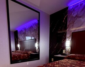 Guest room with large wall mirror, bed with patterned bedding, and accent lighting creating a cozy atmosphere at Imperial Hotel.
