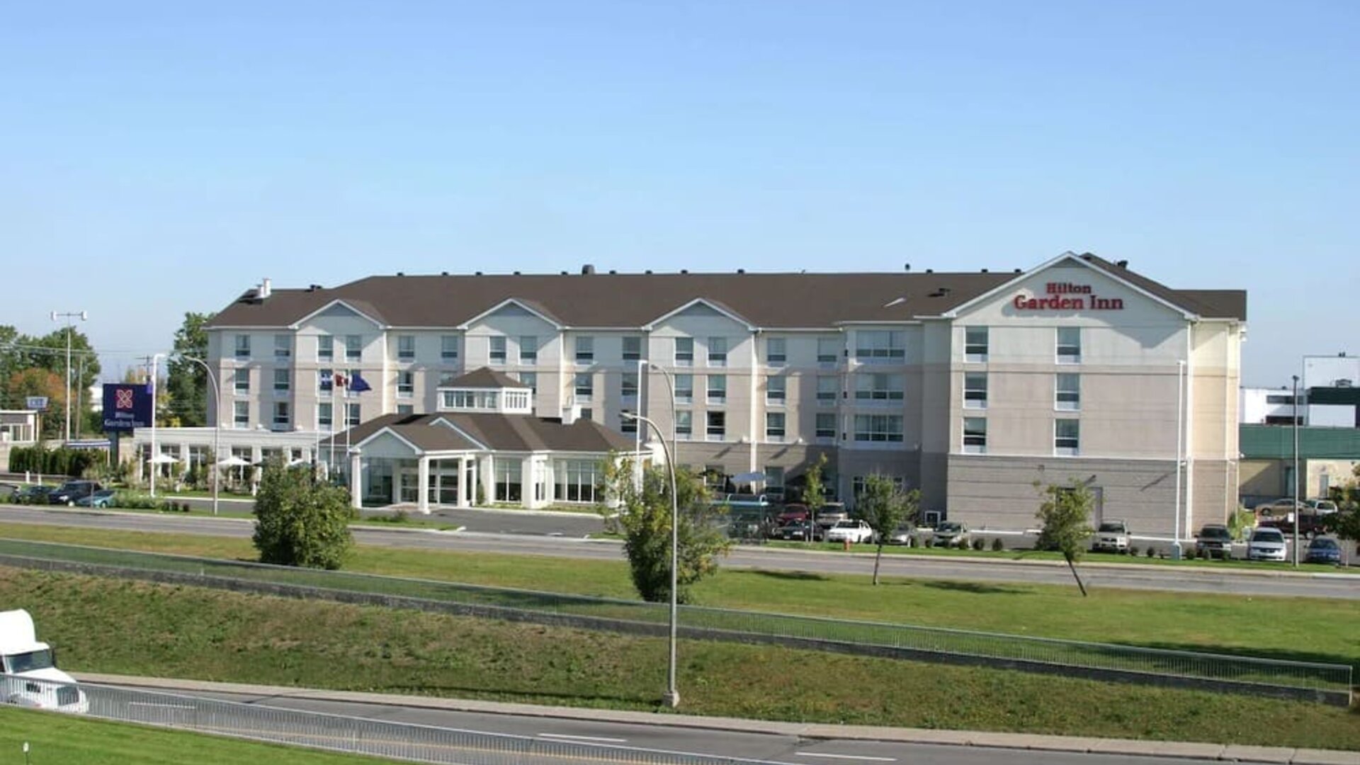 Hotel exterior with green garden at Hilton Garden Inn Montreal Airport.