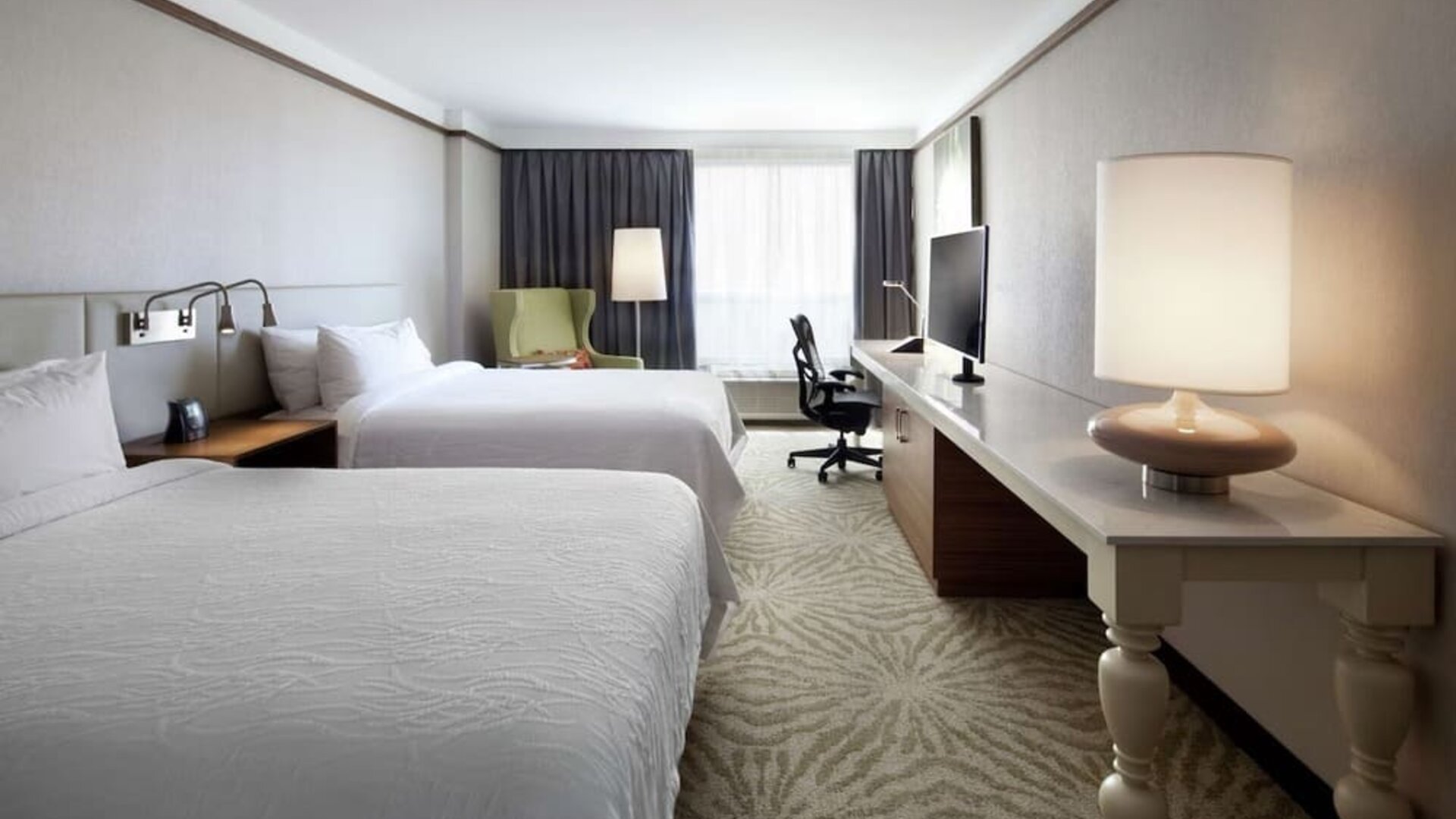 Day use room with two beds, table, lampshade, and work desk at Hilton Garden Inn Montreal Airport.
