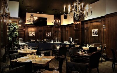 Restaurant dining area with wooden tables, chandeliers, and warm ambient lighting at Holiday Inn New York City - Times Square By IHG.