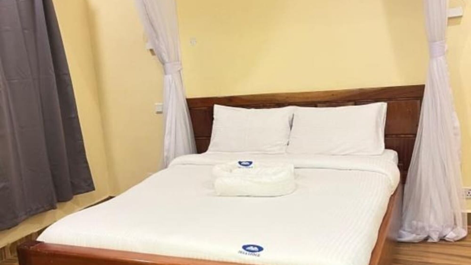 Cozy bedroom at Sega Lodge featuring a wooden bed with white linens, soft canopy drapes, and warm-toned walls.