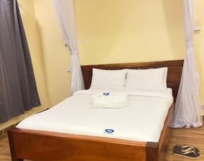 Cozy bedroom at Sega Lodge featuring a wooden bed with white linens, soft canopy drapes, and warm-toned walls.