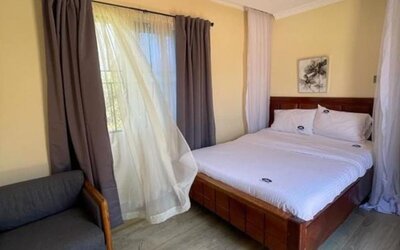 Bright guest room with a canopy-style bed, large window with sheer and blackout curtains, and a comfortable seating area at Sega Lodge.