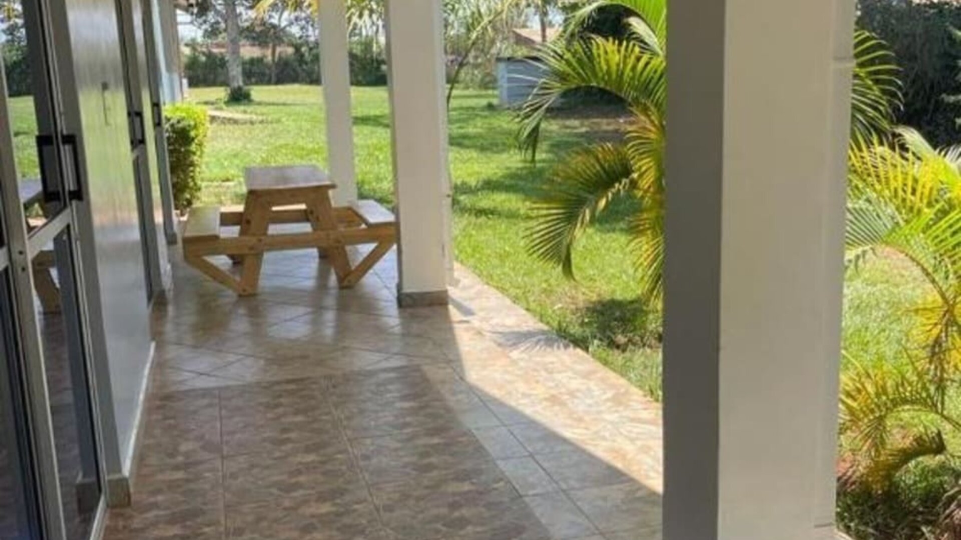 Covered patio area with tiled flooring and picnic-style seating, overlooking the garden at Sega Lodge.