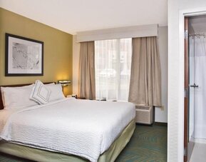 Guest room with king bed, white bedding, window with curtains and an armchair at Marriott SpringHill Suites Naperville/Warrenville.