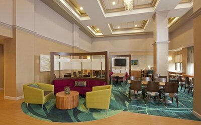 Bright lobby seating area with colorful chairs, round table, and dining tables under coffered ceiling at Marriott SpringHill Suites Naperville/Warrenville.