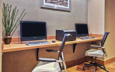 Business center with two desktop computers, keyboard and mouse setups, wood desk, and office chairs against textured wall at Marriott SpringHill Suites Naperville/Warrenville.