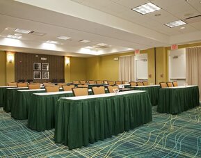 Meeting room with rows of tables draped in green cloths, padded chairs, patterned carpet, and exit doors at Marriott SpringHill Suites Naperville/Warrenville.