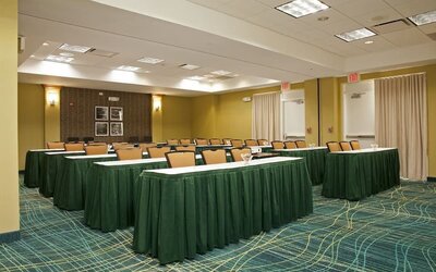 Meeting room with rows of tables draped in green cloths, padded chairs, patterned carpet, and exit doors at Marriott SpringHill Suites Naperville/Warrenville.