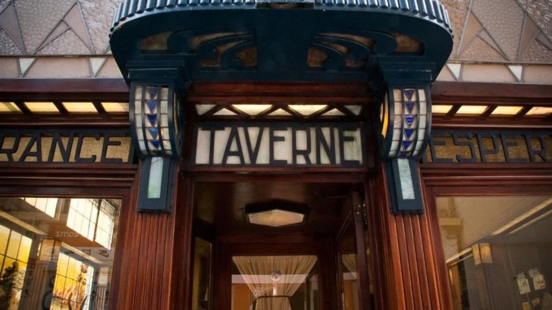 Decorative entrance with ornate wood framing and illuminated signage above glass doorway at Hôtel Espérance.