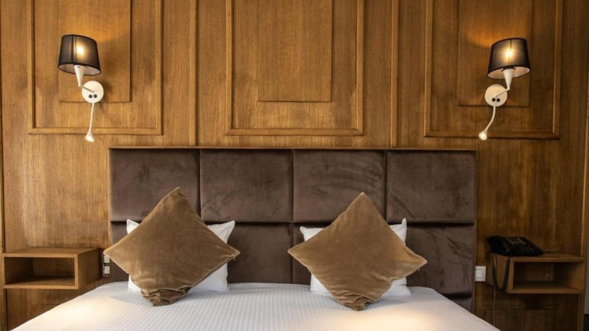 Double bed with padded headboard, wood-paneled wall, and wall-mounted lamps creating a warm, cozy setting at Hôtel Espérance.