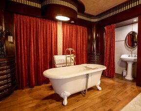 Freestanding clawfoot bathtub with brass fixtures set against red drapes and wood-paneled walls at Hôtel Espérance.