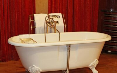 Close-up of vintage clawfoot tub with handheld shower, brass taps, and red curtain backdrop at Hôtel Espérance.