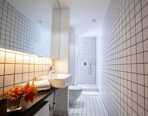 Modern tiled bathroom with wall-mounted sink, toilet, walk-in shower, and minimalist lighting at Hôtel Espérance.