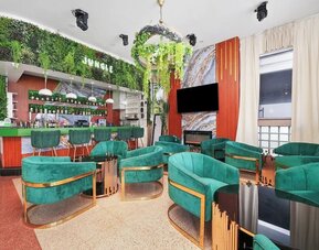 Stylish bar lounge with green velvet chairs, marble accents, hanging plants, and illuminated back bar at Chesterfield Hotel & Suites.