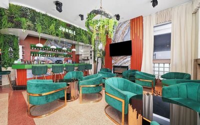 Stylish bar lounge with green velvet chairs, marble accents, hanging plants, and illuminated back bar at Chesterfield Hotel & Suites.