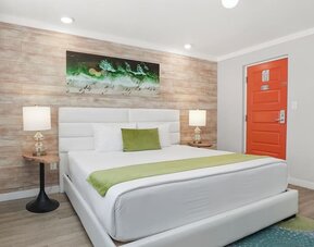 Queen bedroom with upholstered headboard, bedside lamps, artwork, and bright orange entry door at Chesterfield Hotel & Suites.
