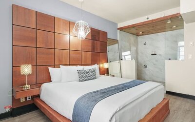 King bedroom with wood-paneled headboard wall, glass-partition shower, and modern lighting at Chesterfield Hotel & Suites.