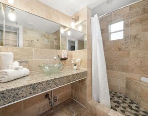 Stone-tiled bathroom with walk-in shower, glass vessel sink on granite counter, and large wall mirror at Chesterfield Hotel & Suites.