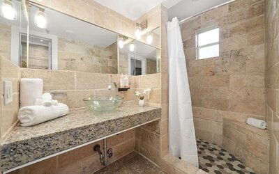 Stone-tiled bathroom with walk-in shower, glass vessel sink on granite counter, and large wall mirror at Chesterfield Hotel & Suites.