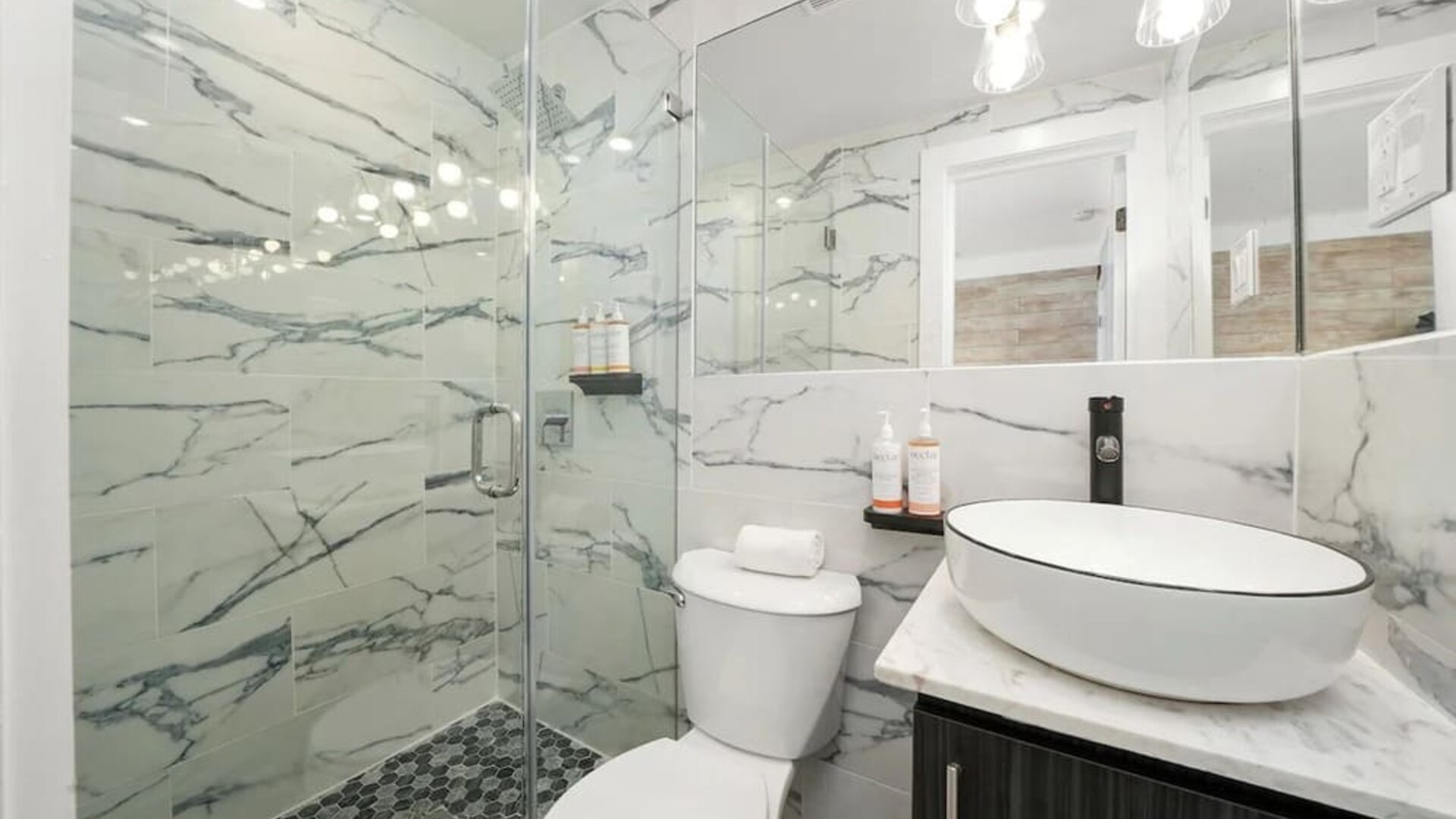 Bright bathroom with marble walls, glass shower enclosure, vessel sink, and mirrored vanity at Chesterfield Hotel & Suites.