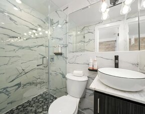 Bright bathroom with marble walls, glass shower enclosure, vessel sink, and mirrored vanity at Chesterfield Hotel & Suites.