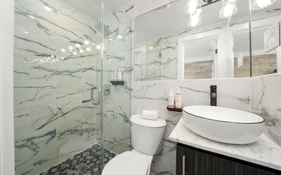 Bright bathroom with marble walls, glass shower enclosure, vessel sink, and mirrored vanity at Chesterfield Hotel & Suites.