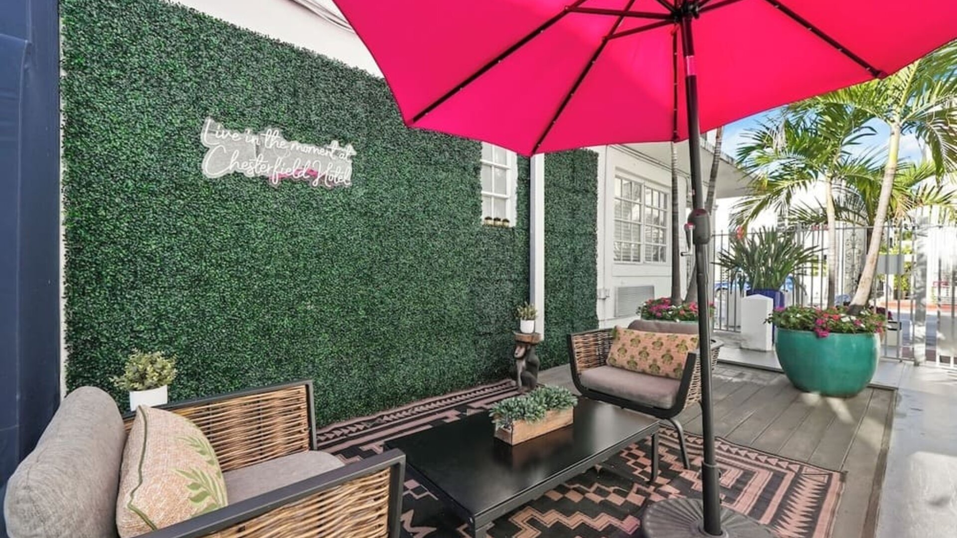 Cozy terrace with cushioned seating, patterned rug, green wall backdrop, and large umbrella at Chesterfield Hotel & Suites.