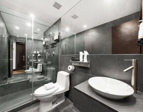 Modern bathroom with dark tile walls, glass shower enclosure, vessel sink, and wall-mounted fixtures at Hotel Chelsea, A South Beach Group Hotel.