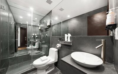 Modern bathroom with dark tile walls, glass shower enclosure, vessel sink, and wall-mounted fixtures at Hotel Chelsea, A South Beach Group Hotel.