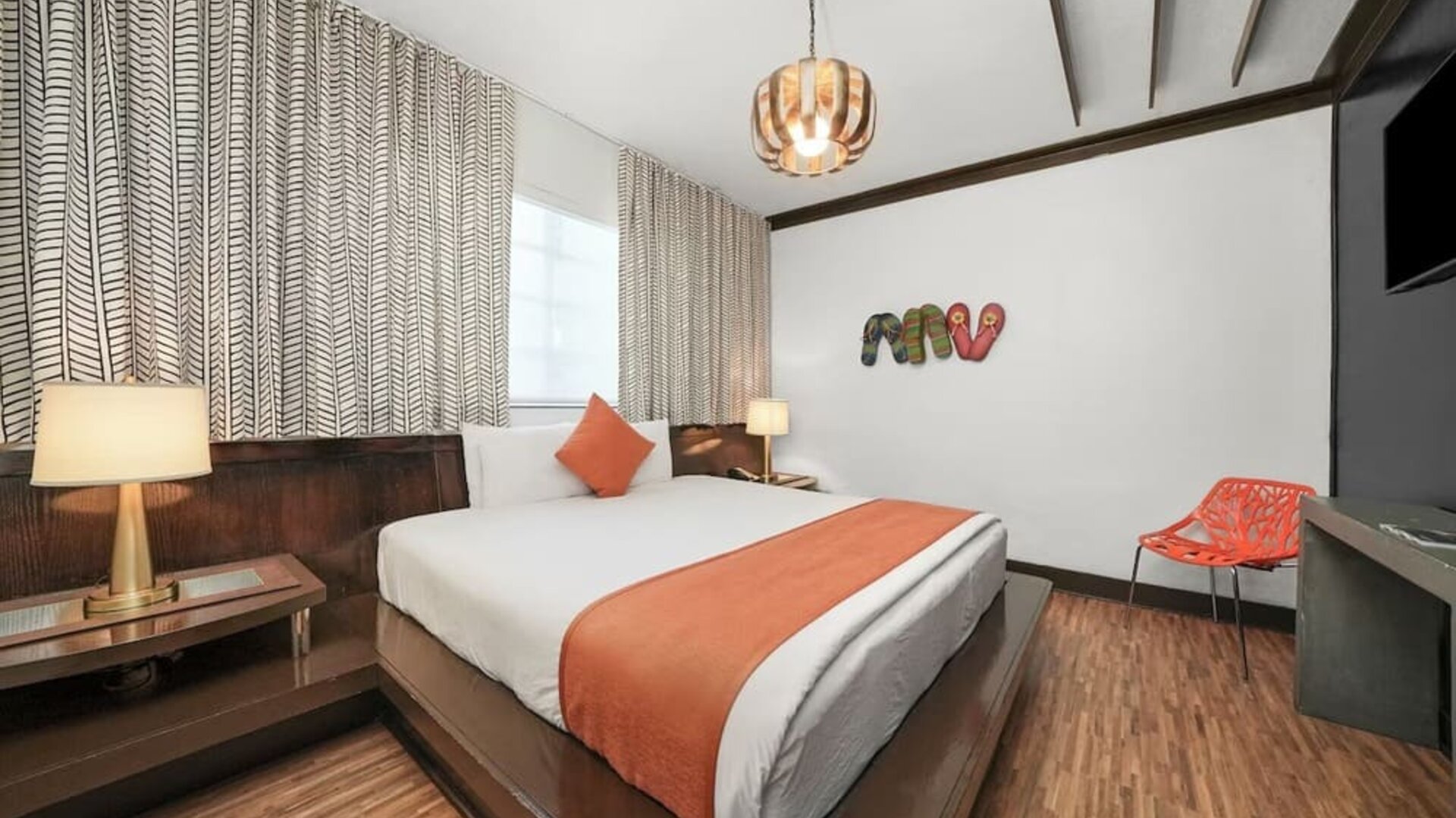 Contemporary guest room with platform bed, orange accents, patterned curtains, and wood flooring at Hotel Chelsea, A South Beach Group Hotel.