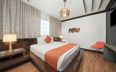 Contemporary guest room with platform bed, orange accents, patterned curtains, and wood flooring at Hotel Chelsea, A South Beach Group Hotel.
