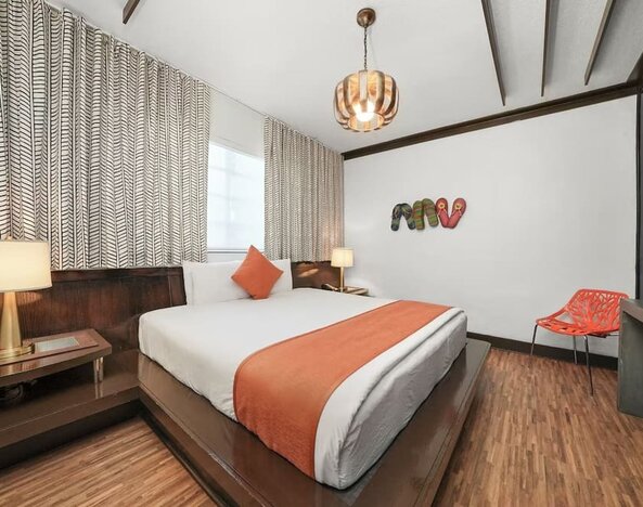 Contemporary guest room with platform bed, orange accents, patterned curtains, and wood flooring at Hotel Chelsea, A South Beach Group Hotel.