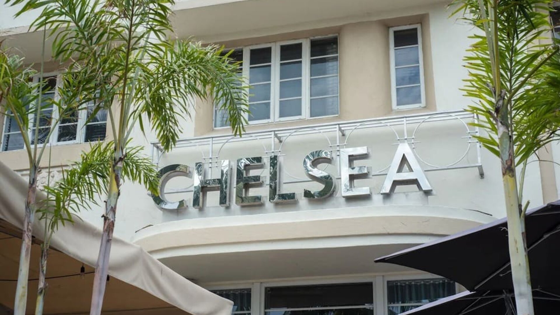 Exterior entrance with large Chelsea signage, palm trees, and shaded outdoor seating area at Hotel Chelsea, A South Beach Group Hotel.