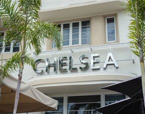 Exterior entrance with large Chelsea signage, palm trees, and shaded outdoor seating area at Hotel Chelsea, A South Beach Group Hotel.