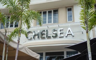 Exterior entrance with large Chelsea signage, palm trees, and shaded outdoor seating area at Hotel Chelsea, A South Beach Group Hotel.