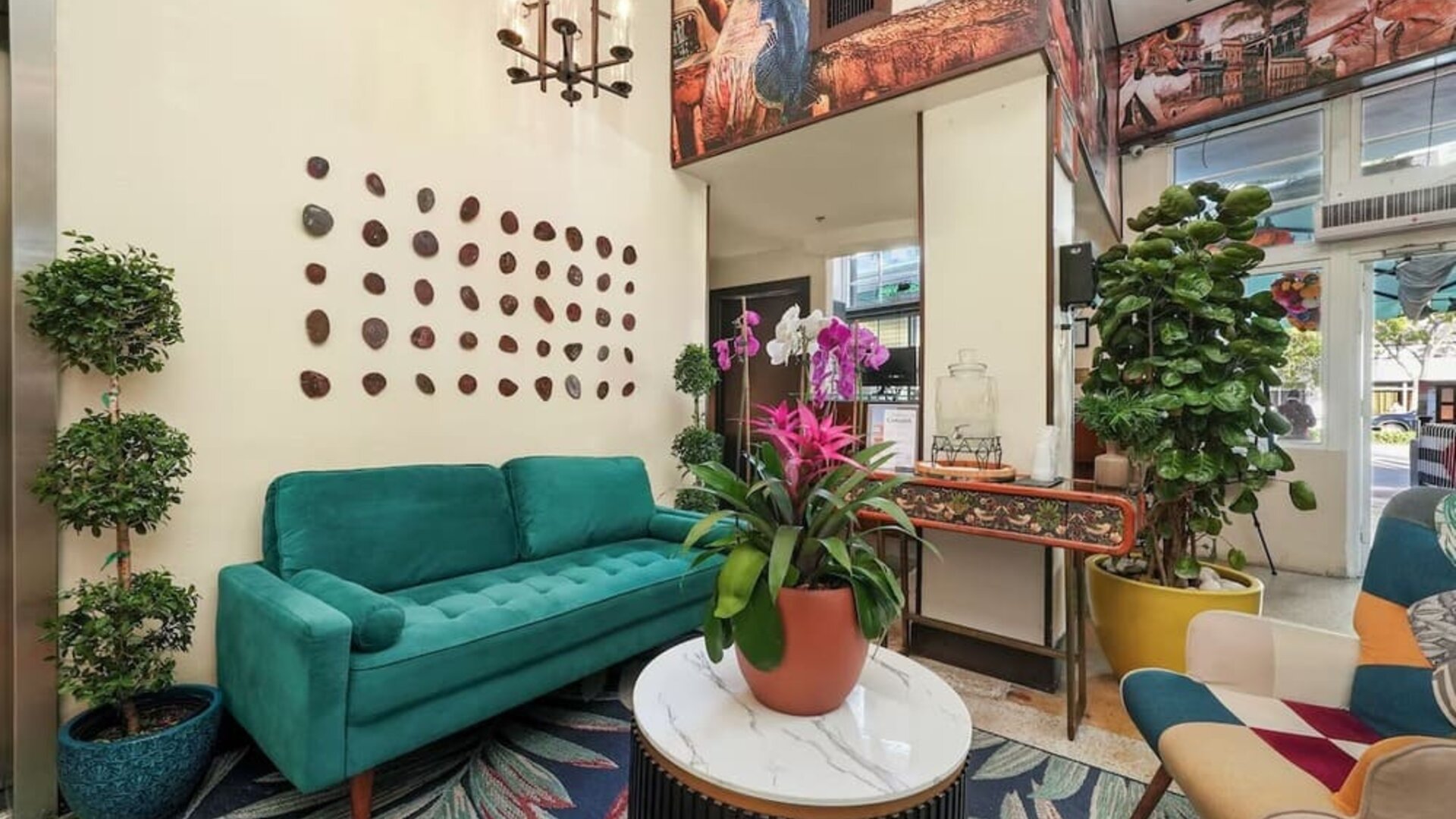 Cozy lobby with green sofa, colorful chairs, patterned rug, plants, and decorative wall art at Hotel Chelsea, A South Beach Group Hotel.