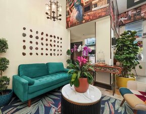 Cozy lobby with green sofa, colorful chairs, patterned rug, plants, and decorative wall art at Hotel Chelsea, A South Beach Group Hotel.
