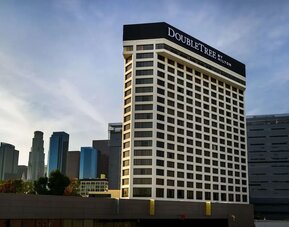 Exterior view of tall hotel building with DoubleTree signage and city skyline backdrop at DoubleTree By Hilton Los Angeles Downtown.