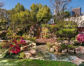 Landscaped garden with pond, wooden bridge, rocks, and colorful flowering plants at DoubleTree By Hilton Los Angeles Downtown.