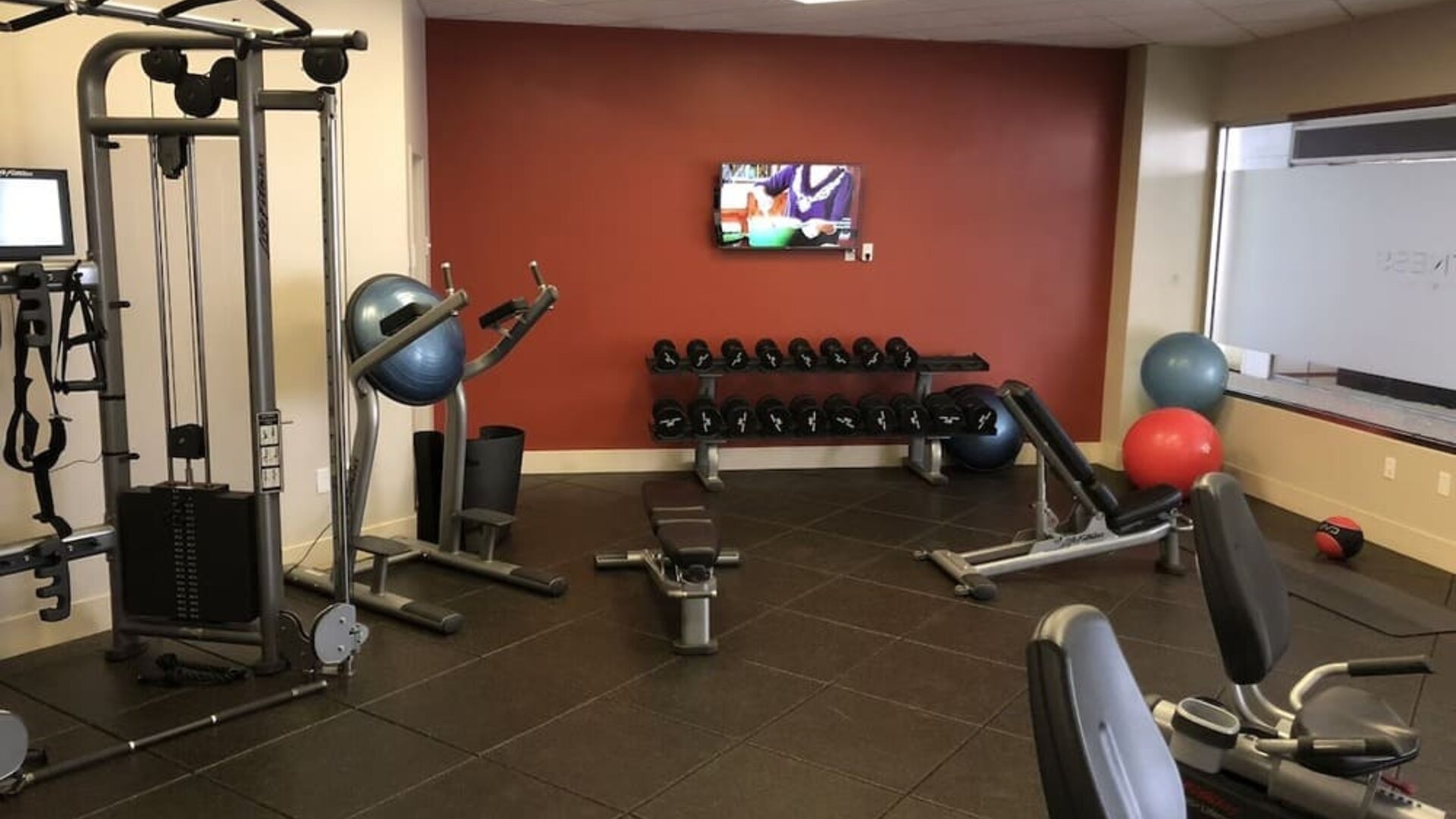 Fitness center with weight machines, dumbbells, exercise balls, and mounted TV at DoubleTree By Hilton Los Angeles Downtown.