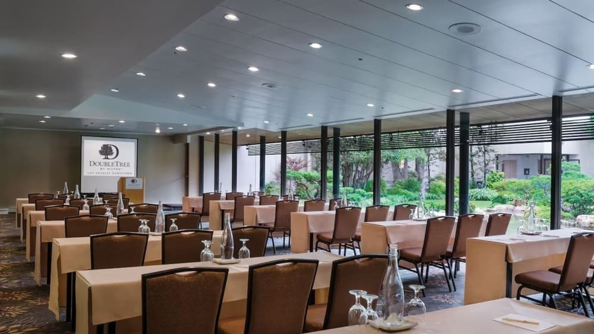 Meeting room with arranged tables, chairs, water bottles, and large windows overlooking greenery at DoubleTree By Hilton Los Angeles Downtown.
