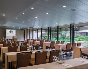 Meeting room with arranged tables, chairs, water bottles, and large windows overlooking greenery at DoubleTree By Hilton Los Angeles Downtown.