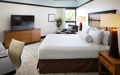 Guest room with king bed, TV console, seating chair, and large window bringing in natural light at The Ambrose Hotel Santa Monica.
