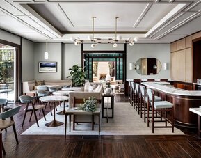 Elegant dining area with marble tables, bar seating, modern chandelier, and soft neutral tones at The Ambrose Hotel Santa Monica.