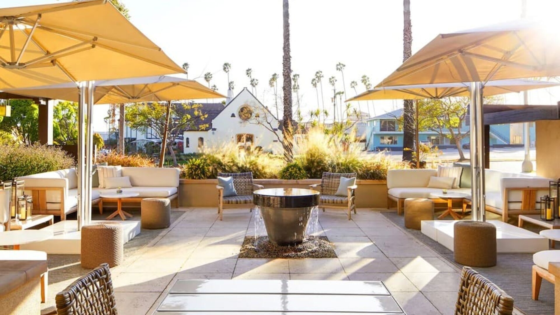 Outdoor patio with lounge seating, umbrellas, fire pit, and landscaped surroundings in soft daylight at The Ambrose Hotel Santa Monica.