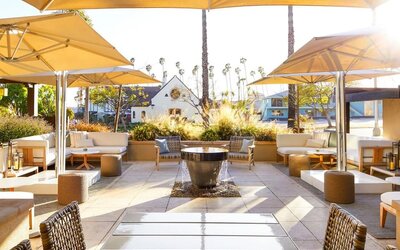 Outdoor patio with lounge seating, umbrellas, fire pit, and landscaped surroundings in soft daylight at The Ambrose Hotel Santa Monica.