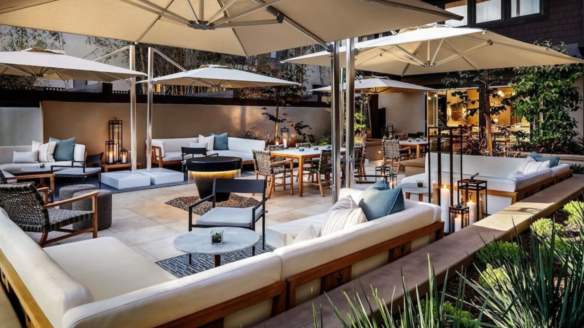 Cozy courtyard patio with cushioned seating, dining tables, umbrellas, and ambient evening lighting at The Ambrose Hotel Santa Monica.