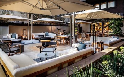 Cozy courtyard patio with cushioned seating, dining tables, umbrellas, and ambient evening lighting at The Ambrose Hotel Santa Monica.