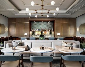 Stylish lounge dining space with cushioned seating, round tables, and backlit bar display at The Ambrose Hotel Santa Monica.